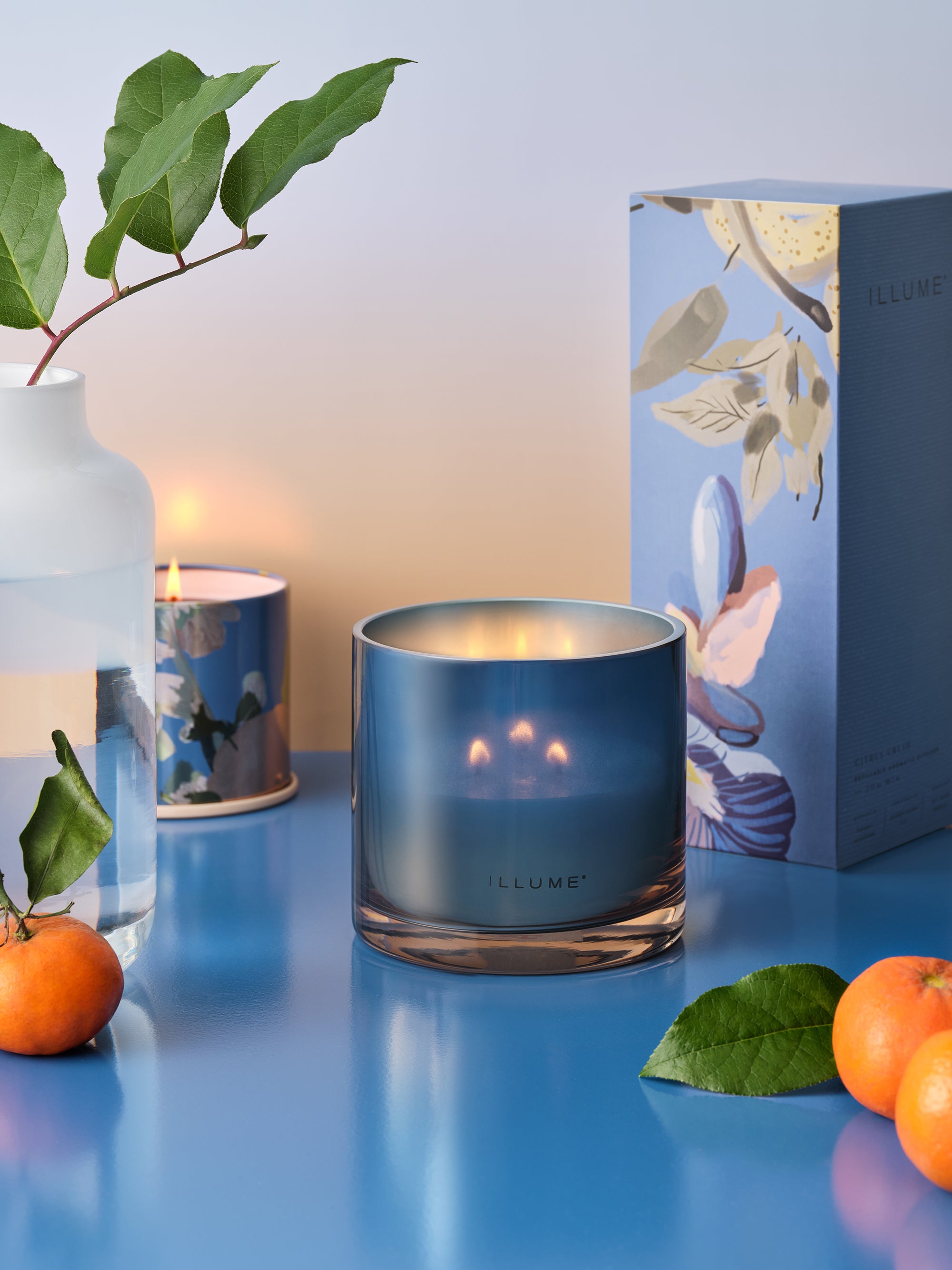 Citrus Crush duftlys i blå tin tændt med citrusfrugter og botanisk gaveæske i baggrunden