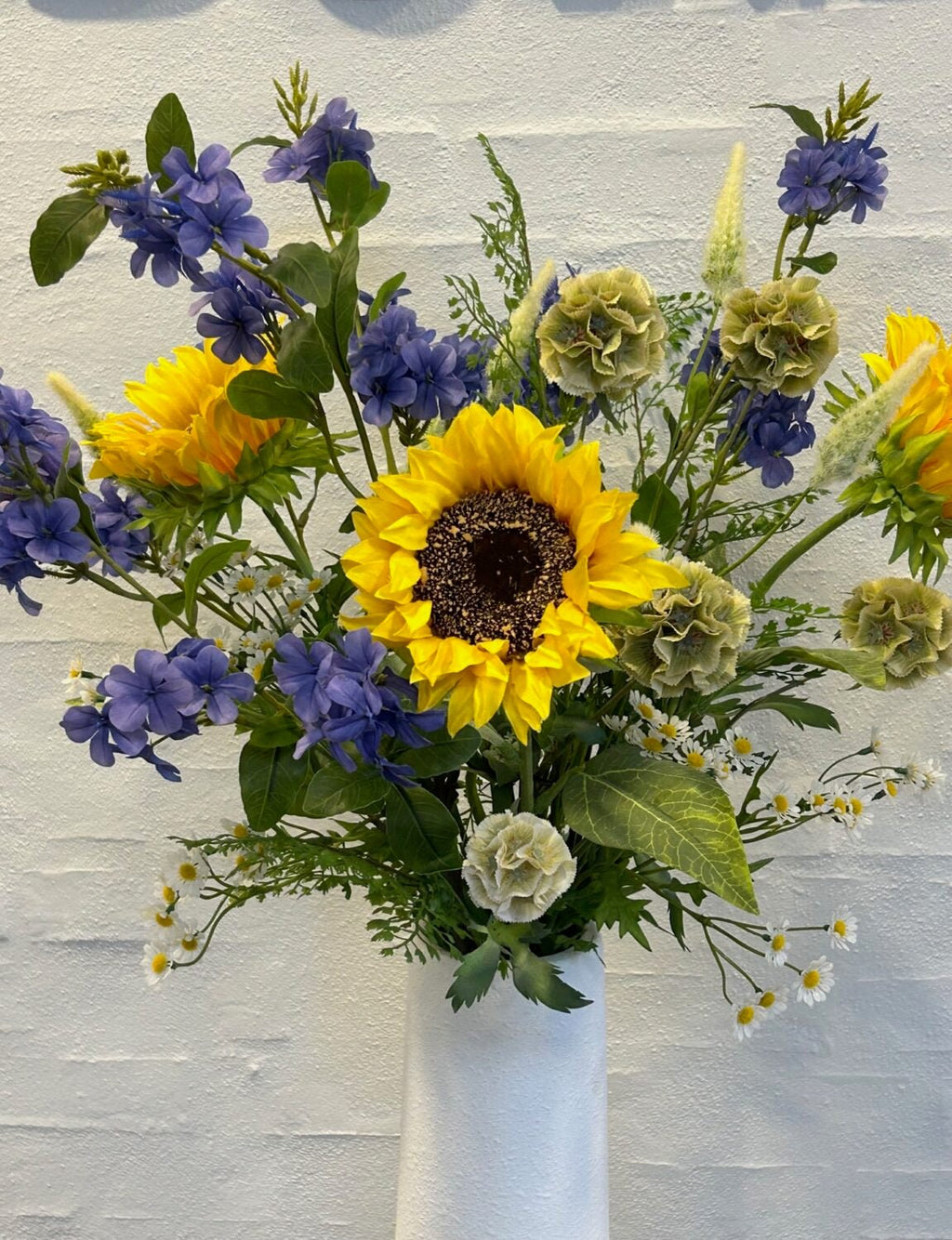 Kunstig solsikke stylet i vase med blå blomster