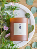 NO. 6 Sequoia duftlys i mørkebrun mat glasbeholder omgivet af blomster og grønne naturlige elementer