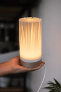 Organis bordlampe tændt med varmt gult lys, holdt i hånd – organisk skulpturel form i beige PLA