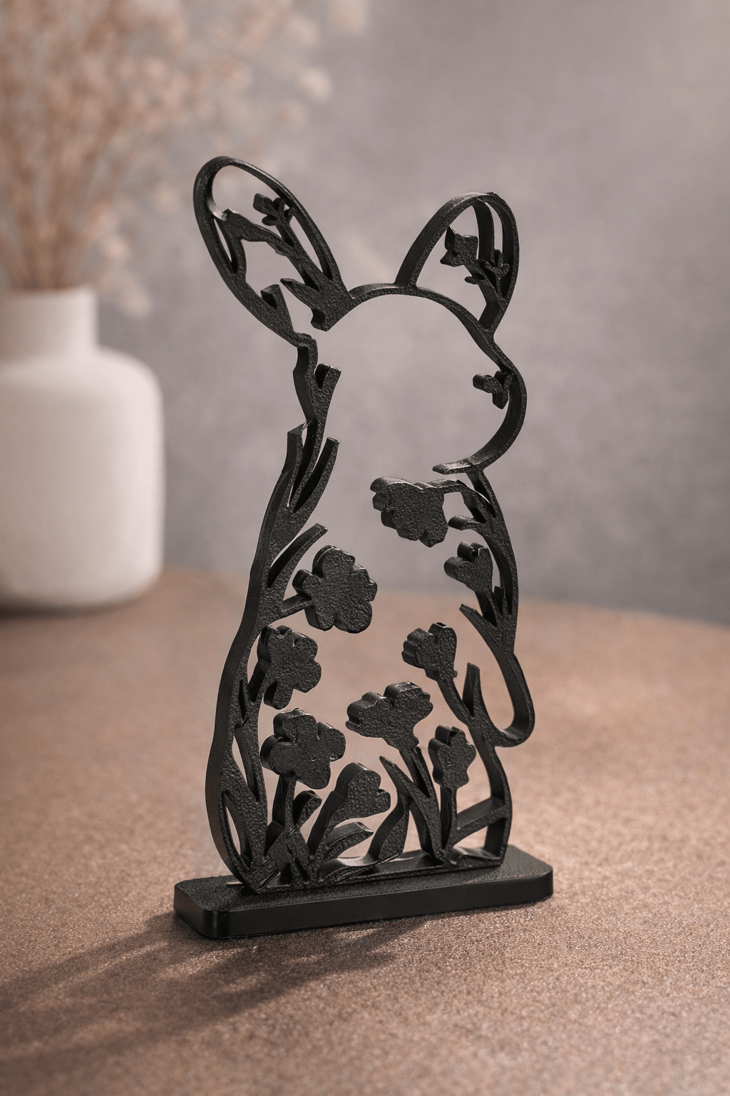 Nærbillede af sort siddende hare skulptur med blomster- og bladudskæringer i kroppen